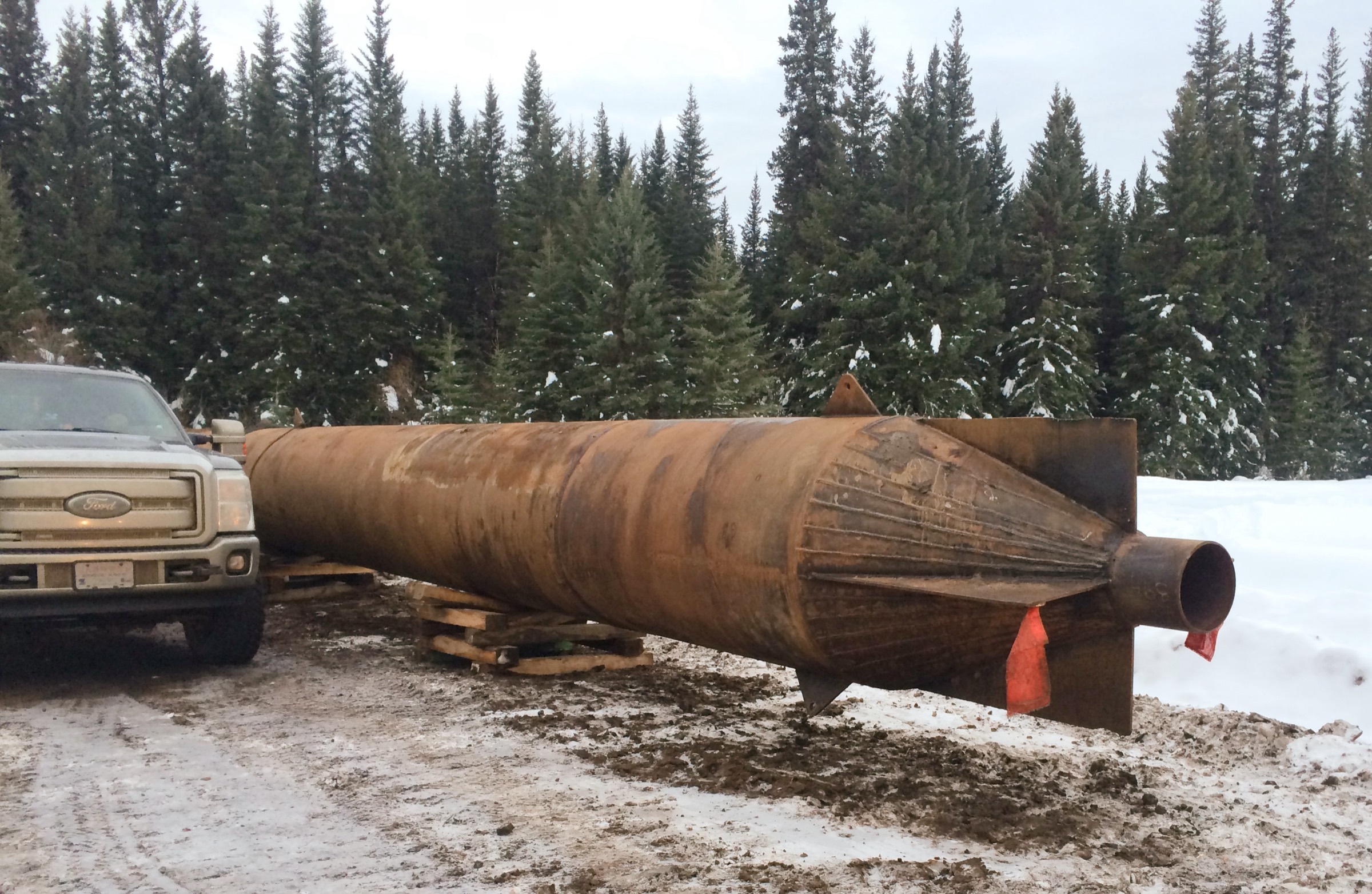 A large steel compaction reamer on skids at the side of a winter lease, the cutting face toward the camera
