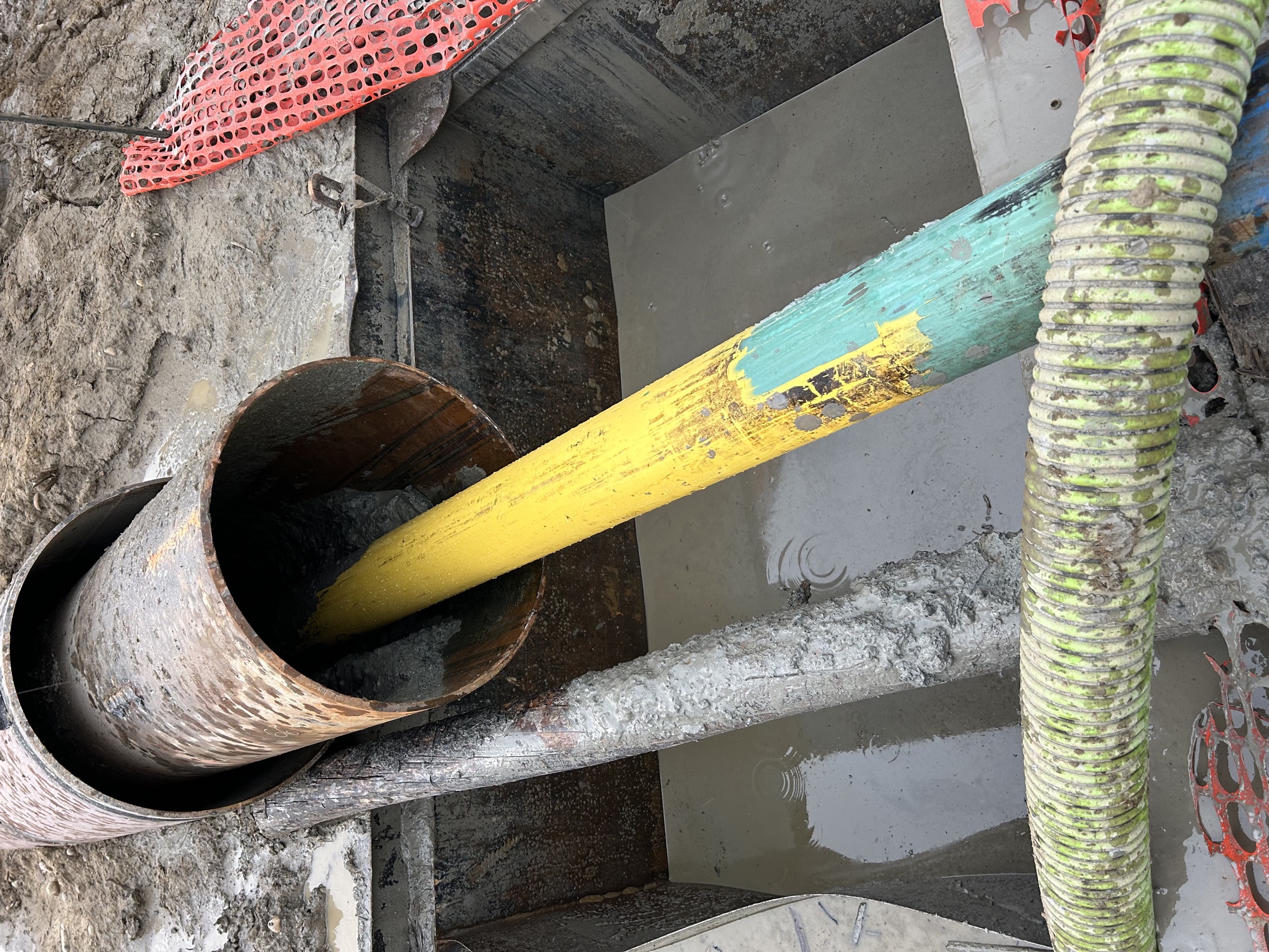 Yellow product pipe emerging from a steel casing at a bore exit, in a bell hole