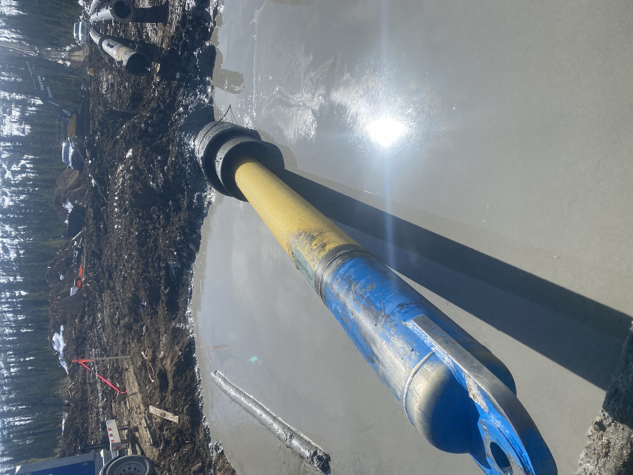 Product pipe on rollers entering open water at a watercourse crossing, drill string under tension