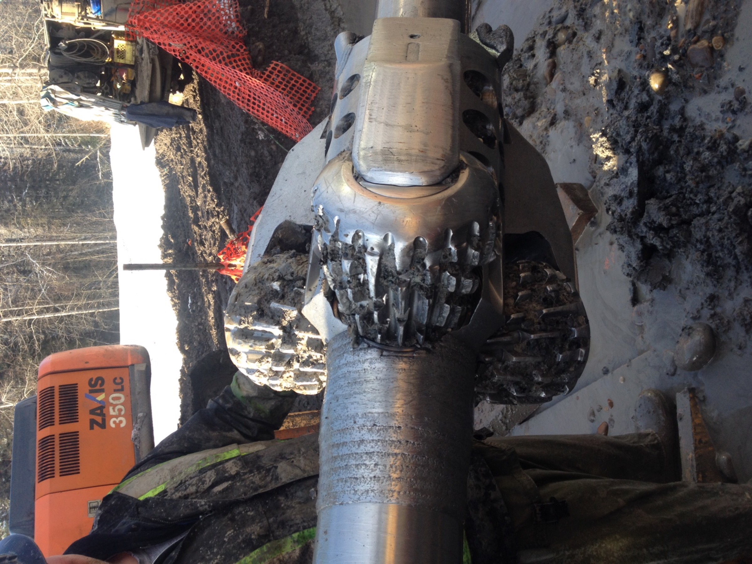 A mud-motor assembly with a tricone rock bit, caked in drilling mud, on the drill string at a bore entry